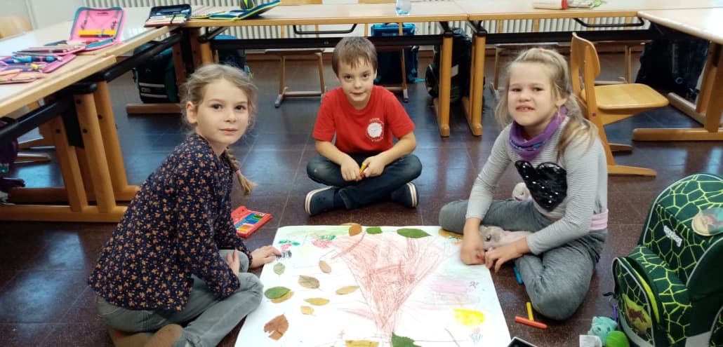 Drei Kinder sitzen auf dem Boden um ein Plakat mit Herbstblättern