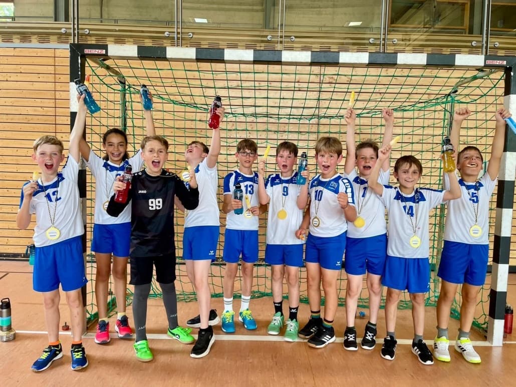 Jubelnde Grundschulmannschaft in Trikots vor dem Handballtor